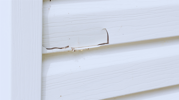 A close-up of damaged siding with visible cracks and moisture stains, showcasing the need for siding repair or replacement.